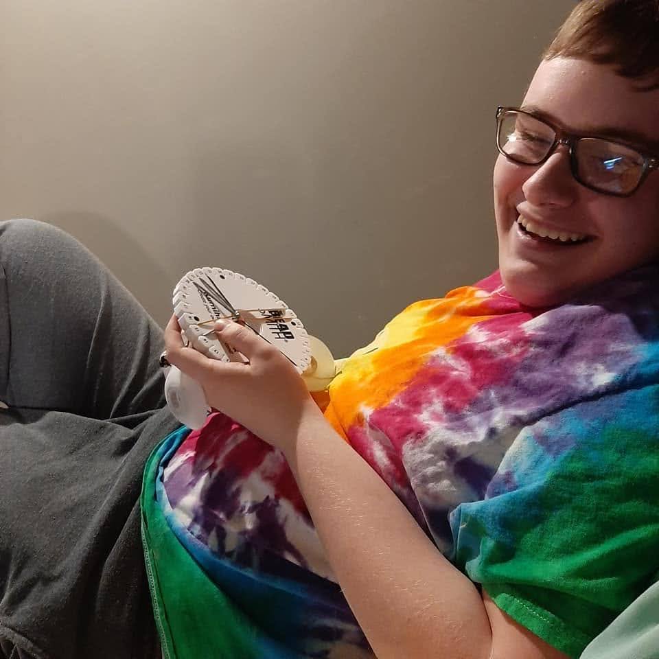 Rhys smiles while braiding cords with a round white Kumihimo disk.